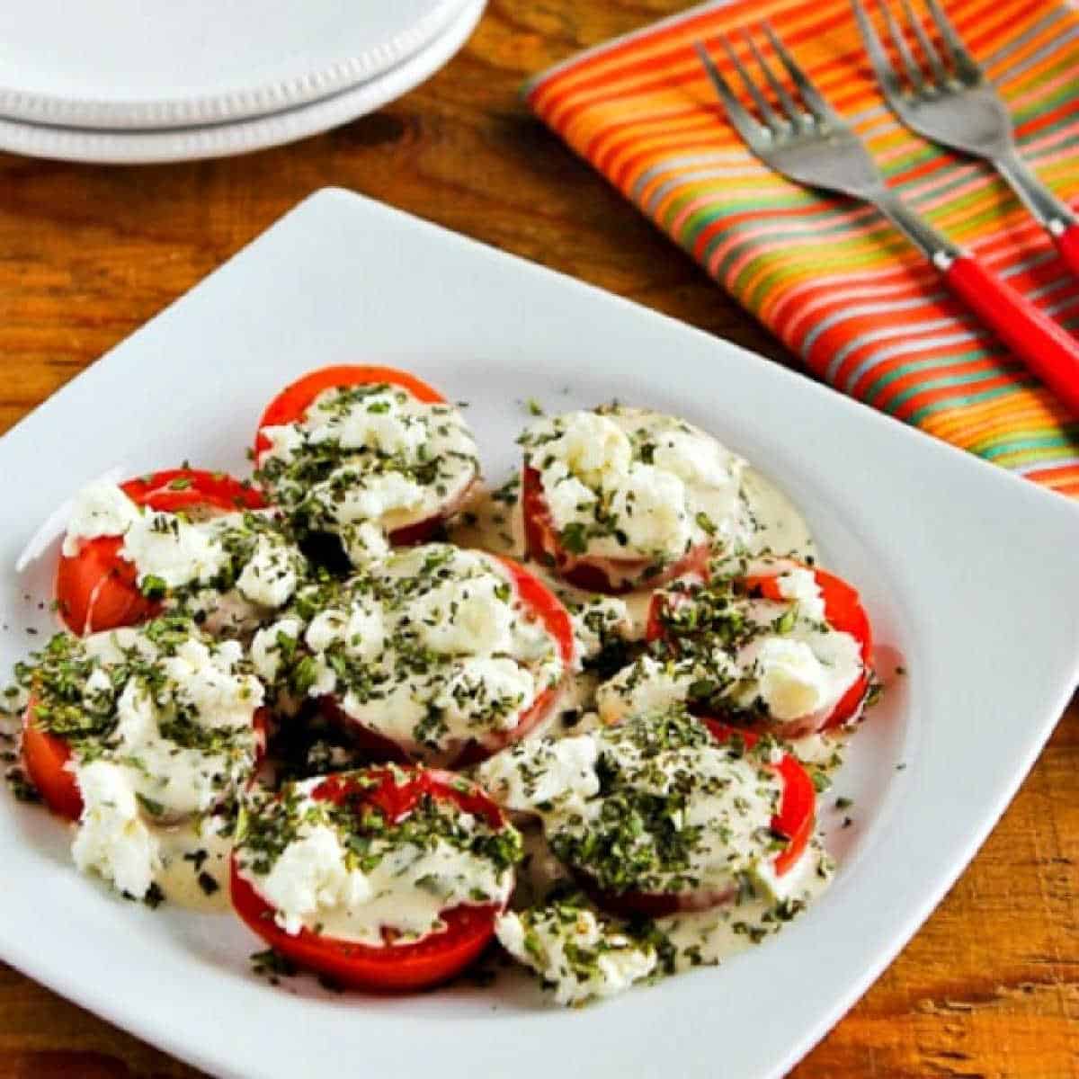 Summer Tomato Salad with Goat Cheese shown on white plate with serving plates, forks, and napkins.