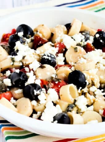 Square image for Tomato Salad with Hearts of Palm, Olives, and Feta shown in white serving bowl.