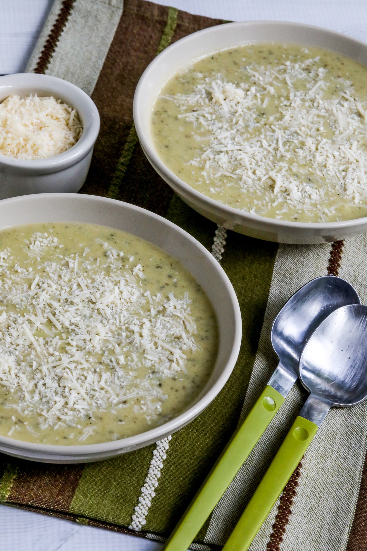 Zucchini and Yellow Squash Soup in two serving bowls with spoons and Parmesan on the side.