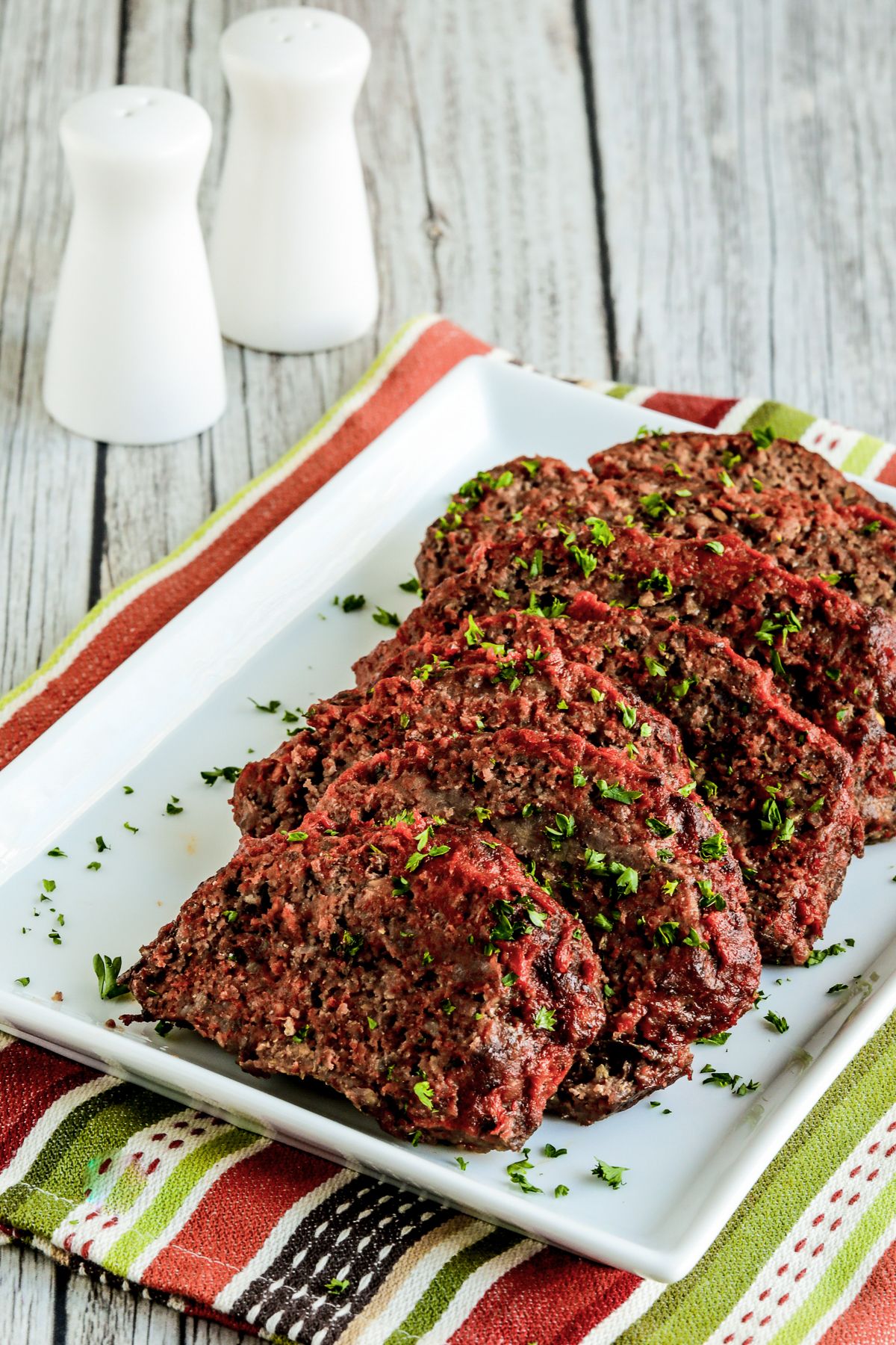 Beef and Sausage Italian Meatloaf on serving plate with salt and pepper in background.