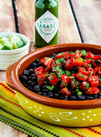 Spicy Black Beans with Cilantro shown in serving bowl with limes and Green Tabasco Sauce.