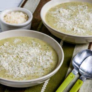 Square image for Zucchini and Yellow Squash Soup in two bowls with spoons and Parmesan.