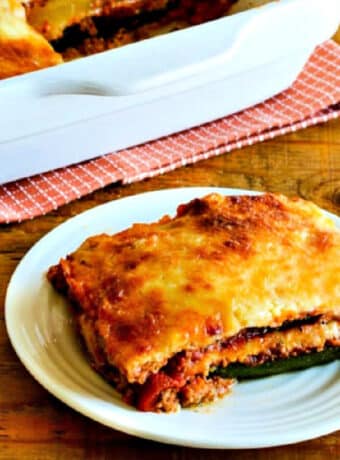 Square image of zucchini lasagna on serving plate with baking dish in back.