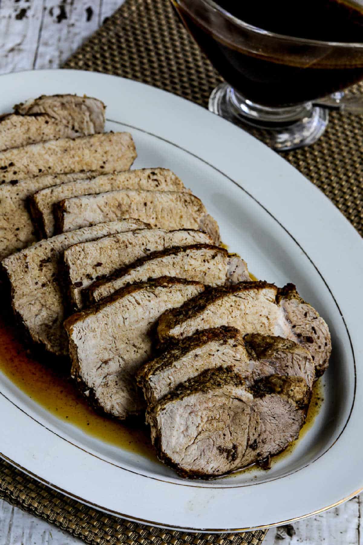 Instant Pot Balsamic Pork Roast on serving platter with formal napkin and sauce boat in background