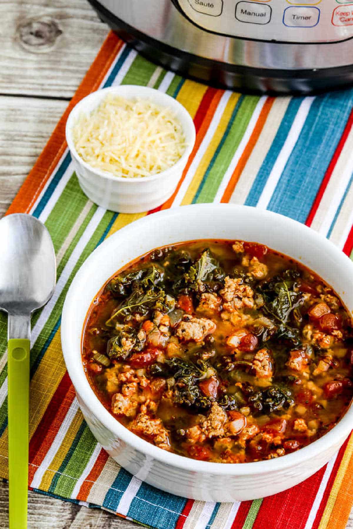 Instant Pot Sausage and Kale Soup shown in serving bowl with Parmesan and Instant Pot in background
