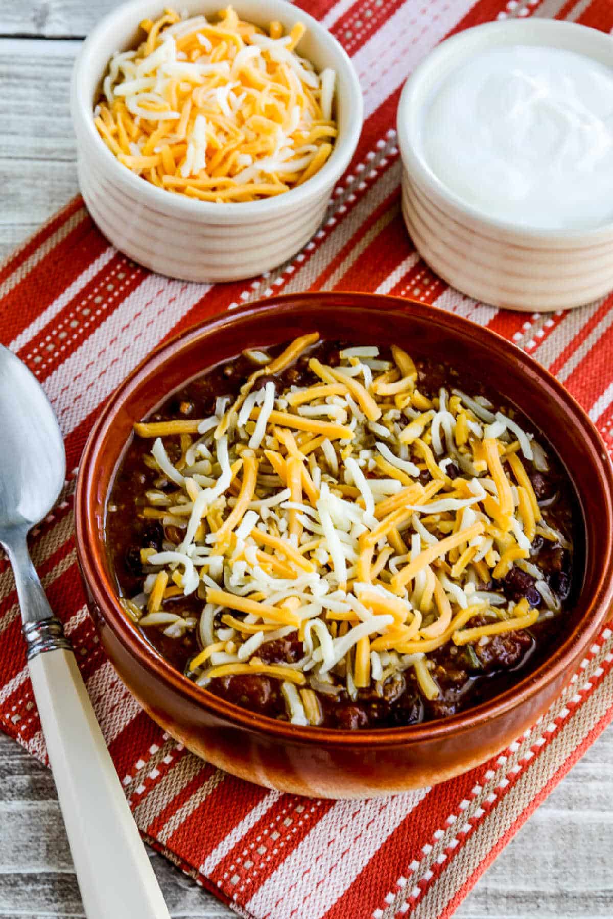 Pumpkin Chili with Ground Beef in serving bowl with cheese, with cheese and sour cream on the side