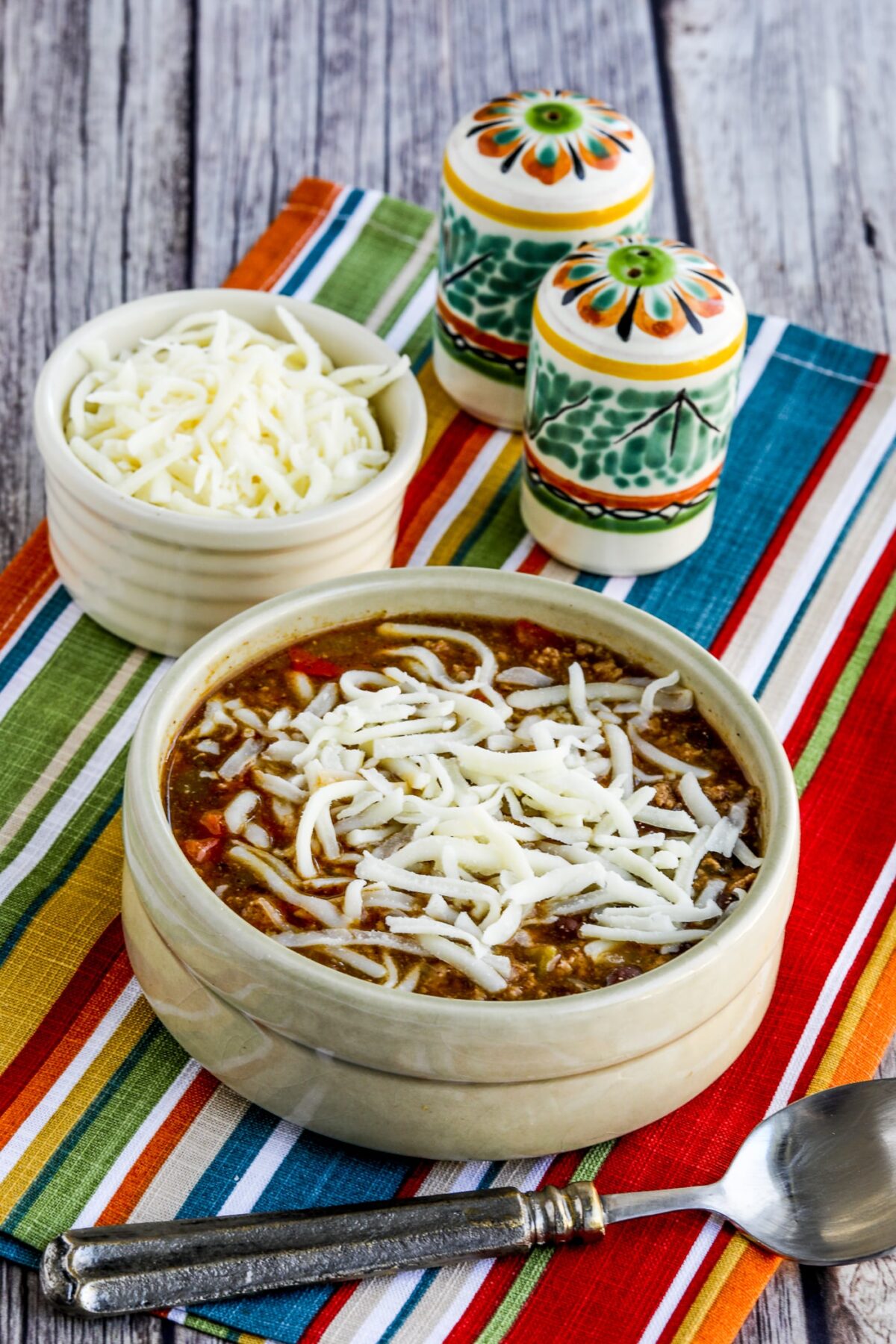 Green Chile Turkey Enchilada Soup shown in serving bowl with cheese and Mexican salt-pepper shakers