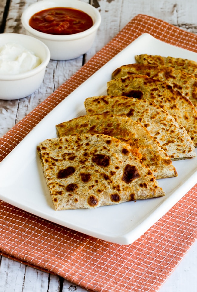 Green Chile Chicken Quesadillas on serving plate with sour cream and salsa in background