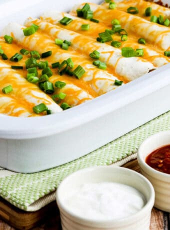 Square image of Egg Burritos for a Crowd with burritos in Casserole CrockPot, and sour cream and salsa on the side.