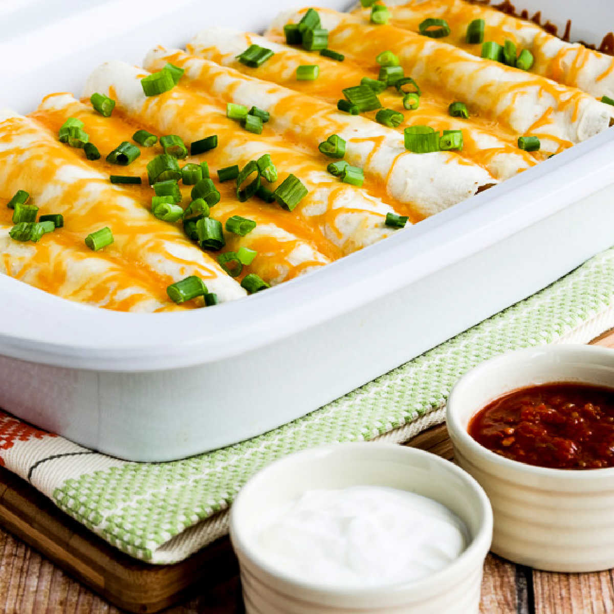 Square image of Egg Burritos for a Crowd with burritos in Casserole CrockPot, and sour cream and salsa on the side.