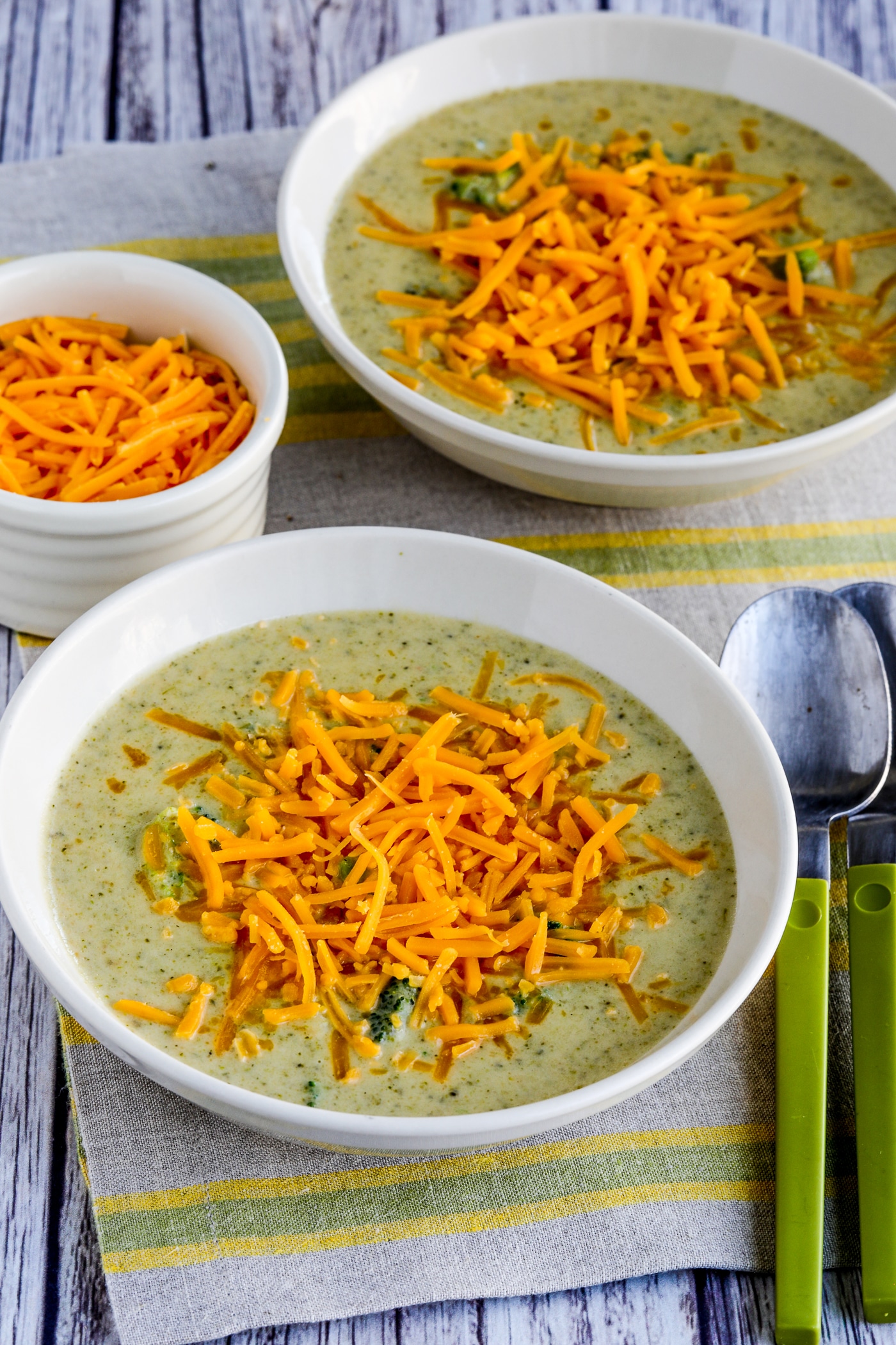 Cheesy Broccoli and Cauilflower Soup shown in two serving bowls with cheese