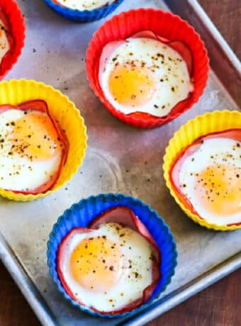 Baked Eggs in Canadian Bacon Cups shown on baking sheet, square image