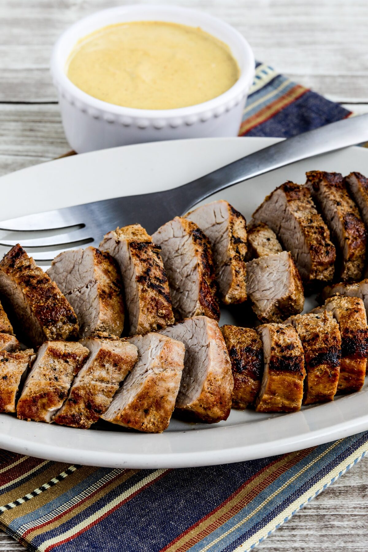 pork tenderloin on serving plate with mustard sauce in background