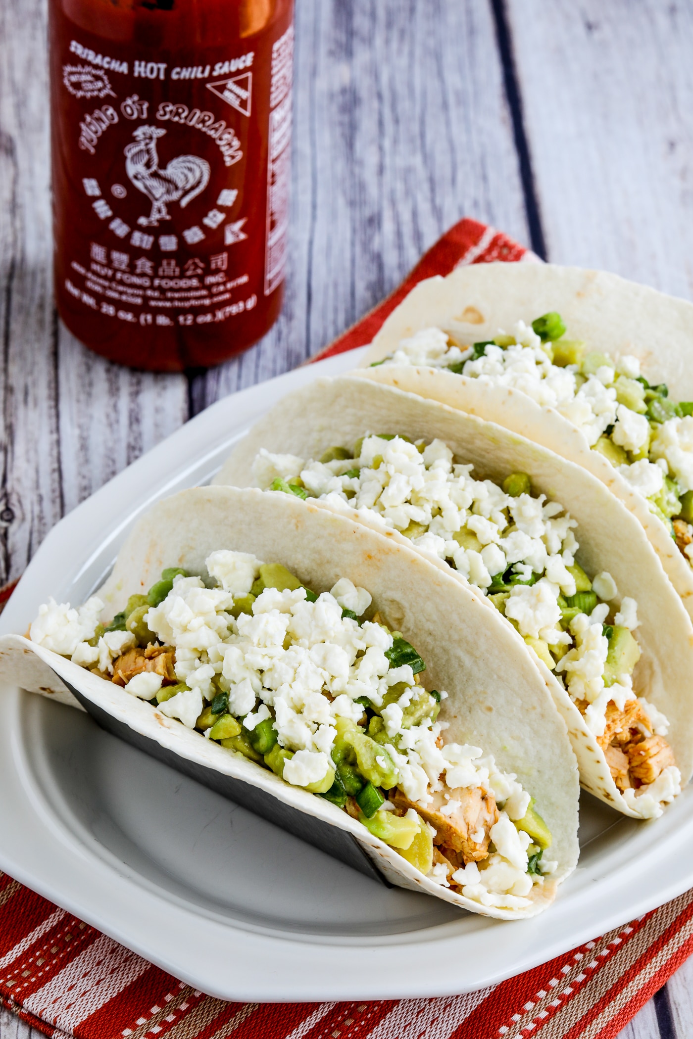 Instant Pot Sriracha Chicken Tacos finished tacos with Queso Fresca and Sriracha bottle in back