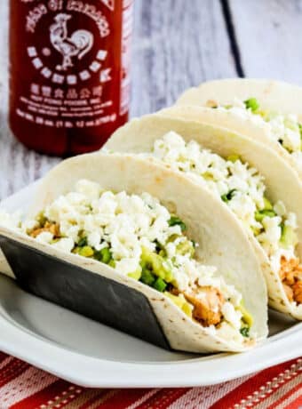 Square image for Instant Pot Sriracha Chicken Tacos on plate with bottle of Sriracha in back.