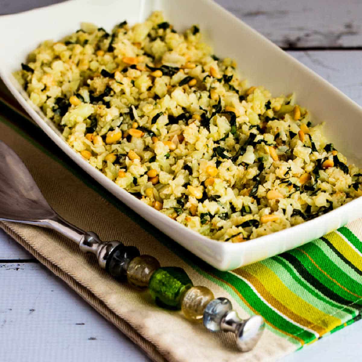 Square image of Cauliflower Rice with Basil, Parmesan, and Pine Nuts in serving bowl on napkin.