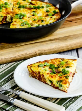 Square image of Bacon Frittata with Two Cheeses shown with one slice on plate and frittata in back.