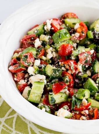 Square image of Tomato Cucumber Salad with Mint and Feta in white bowl on green-white-napkin.
