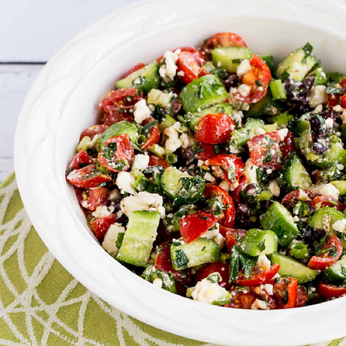 Square image of Tomato Cucumber Salad with Mint and Feta in white bowl on green-white-napkin.