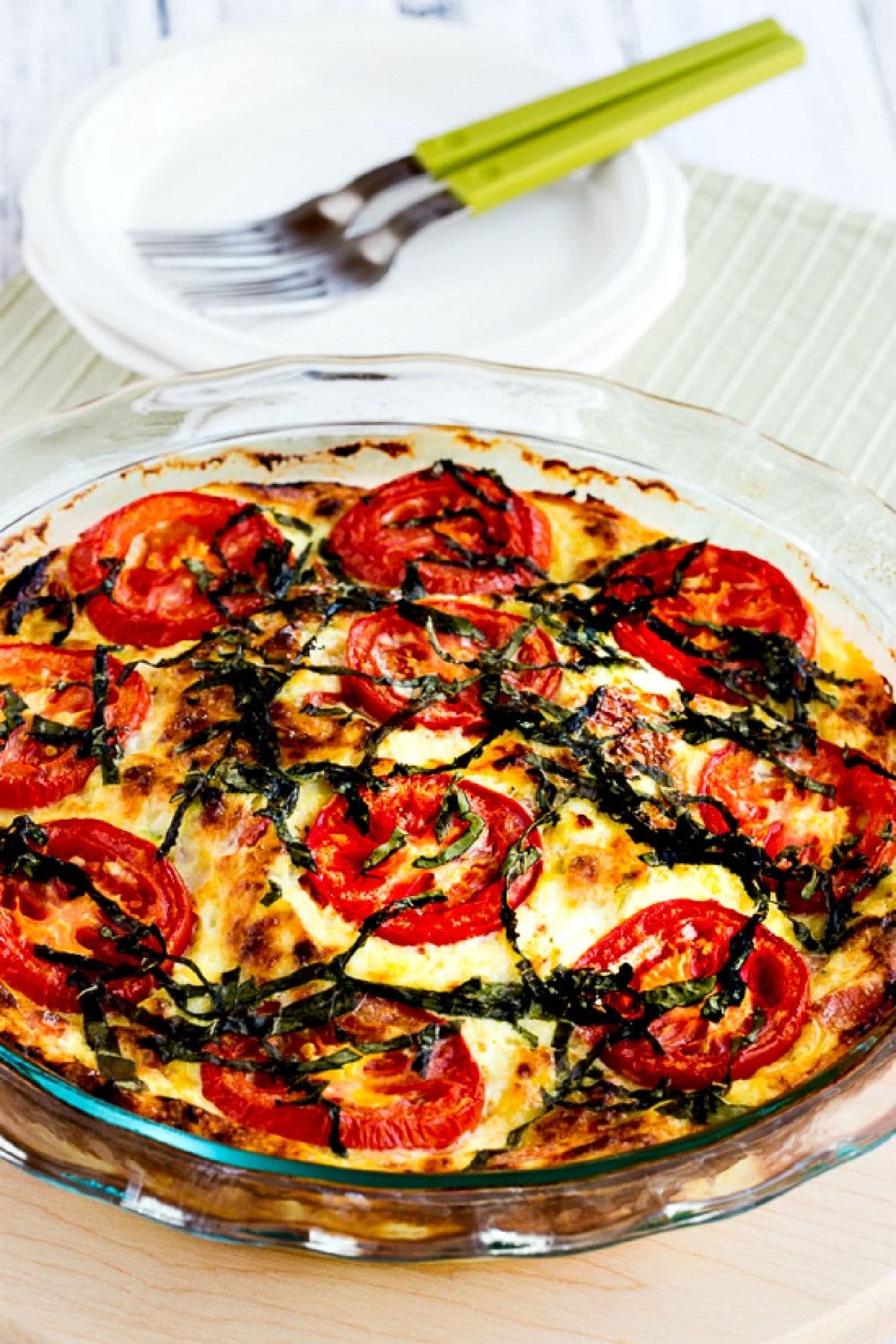 Crustless Three-Cheese Tomato-Basil Quiche shown in baking dish with plates-forks in background