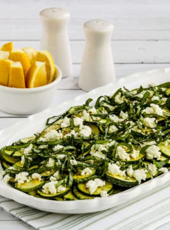 Square image of Zucchini Carpaccio on serving dish with lemon in background.