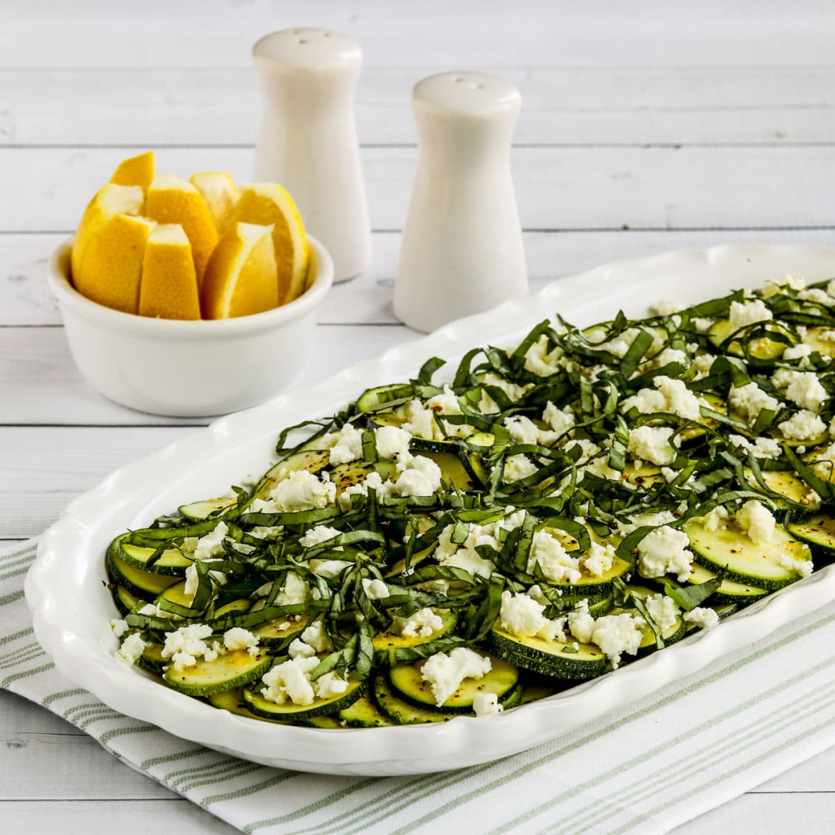 Square image of Zucchini Carpaccio on serving dish with lemon in background.