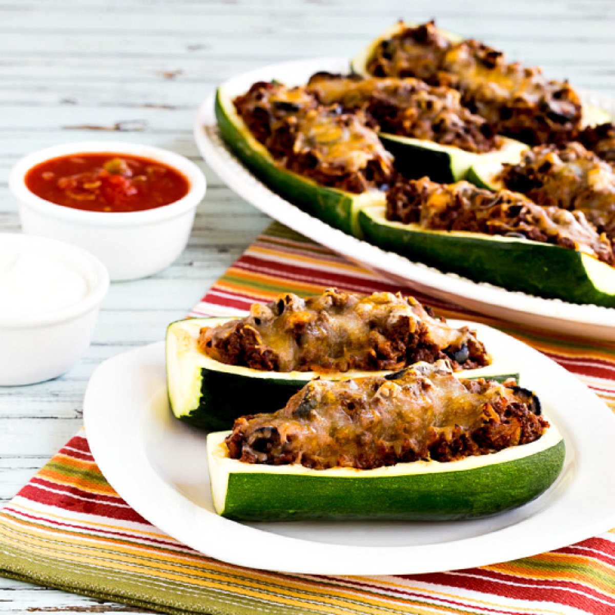 square image of Taco Zucchini Boats on serving plate and platter with salsa on the side