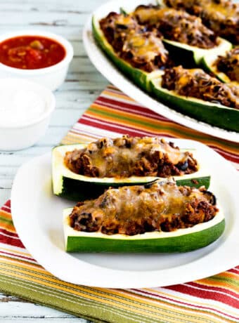 Taco Zucchini Boats with two on serving plate and platter in background