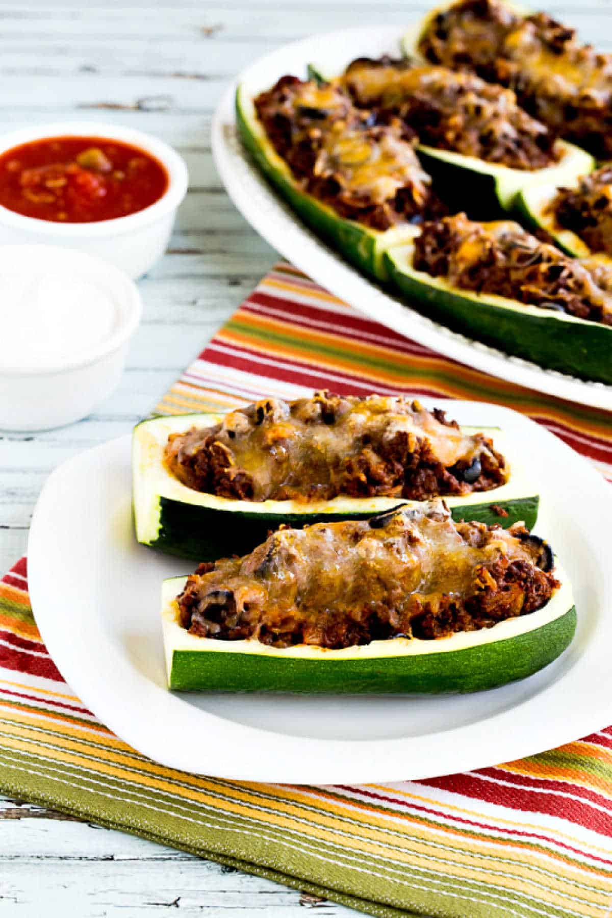 Taco Zucchini Boats with two on serving plate and platter in background