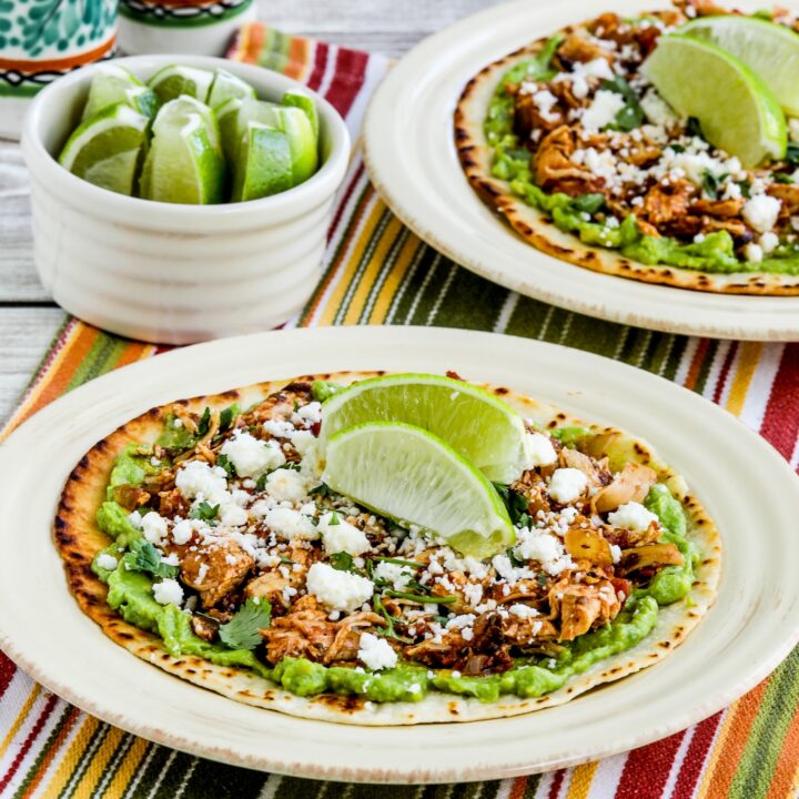 Instant Pot Chicken Tinga served on tostada with guacamole and limes in the backround