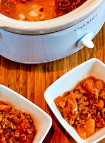 Square image of Slow Cooker Peach Crisp shown in two serving bowls with slow cooker in back.