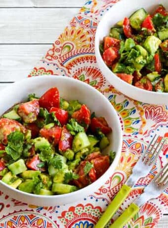 Square image of Tomato Salad with Cucumber, Avocado, and Cilantro in two bowls with forks.