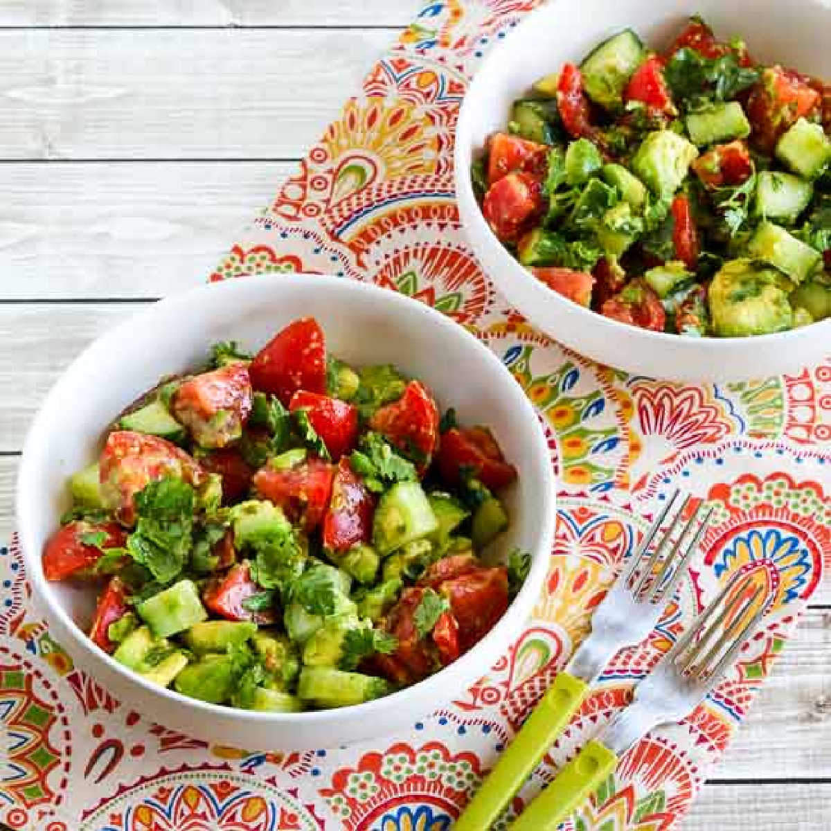 Square image of Tomato Salad with Cucumber, Avocado, and Cilantro in two bowls with forks.