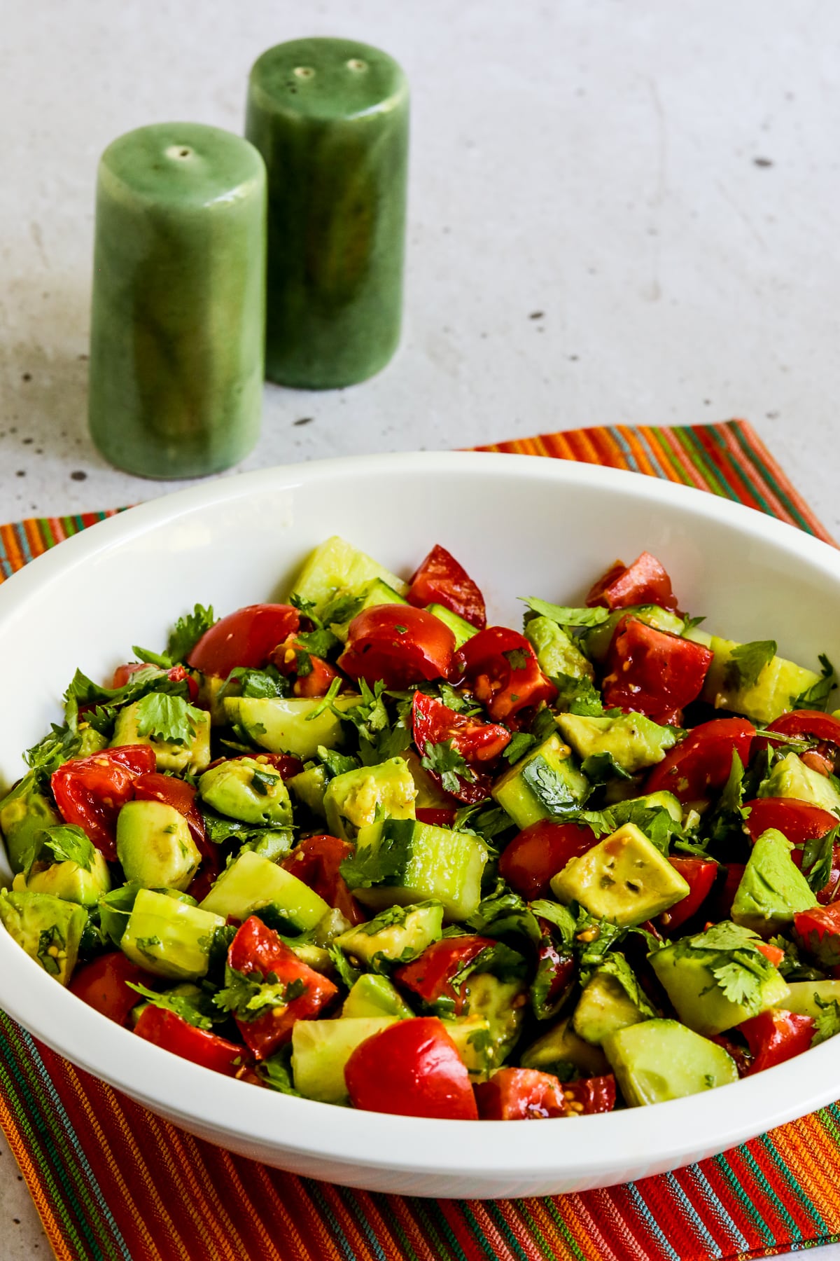 Tomato Salad with Cucumbers, Avocado, and Cilantro in bowl with green salt-pepper shakers.