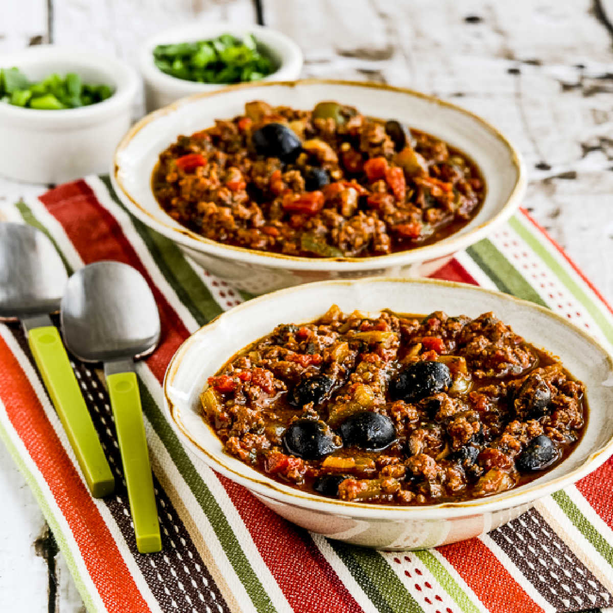 Pumpkin Chili with Beef, Peppers, and Olives in two serving. bowls, square image