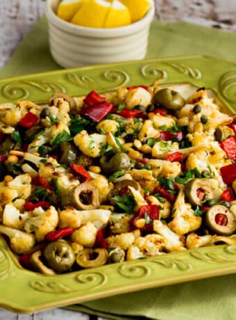 square image of Roasted Cauliflower with Red Peppers, Green Olives, and Pine Nuts shown on green serving plate