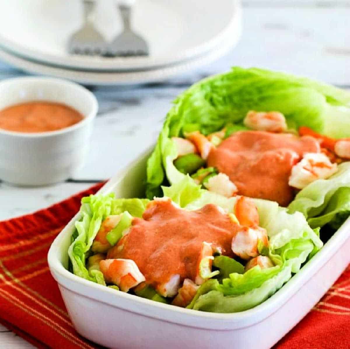 Shrimp lettuce wraps shown with two lettuce wraps in dish with cocktail sauce on the shrimp and on the side