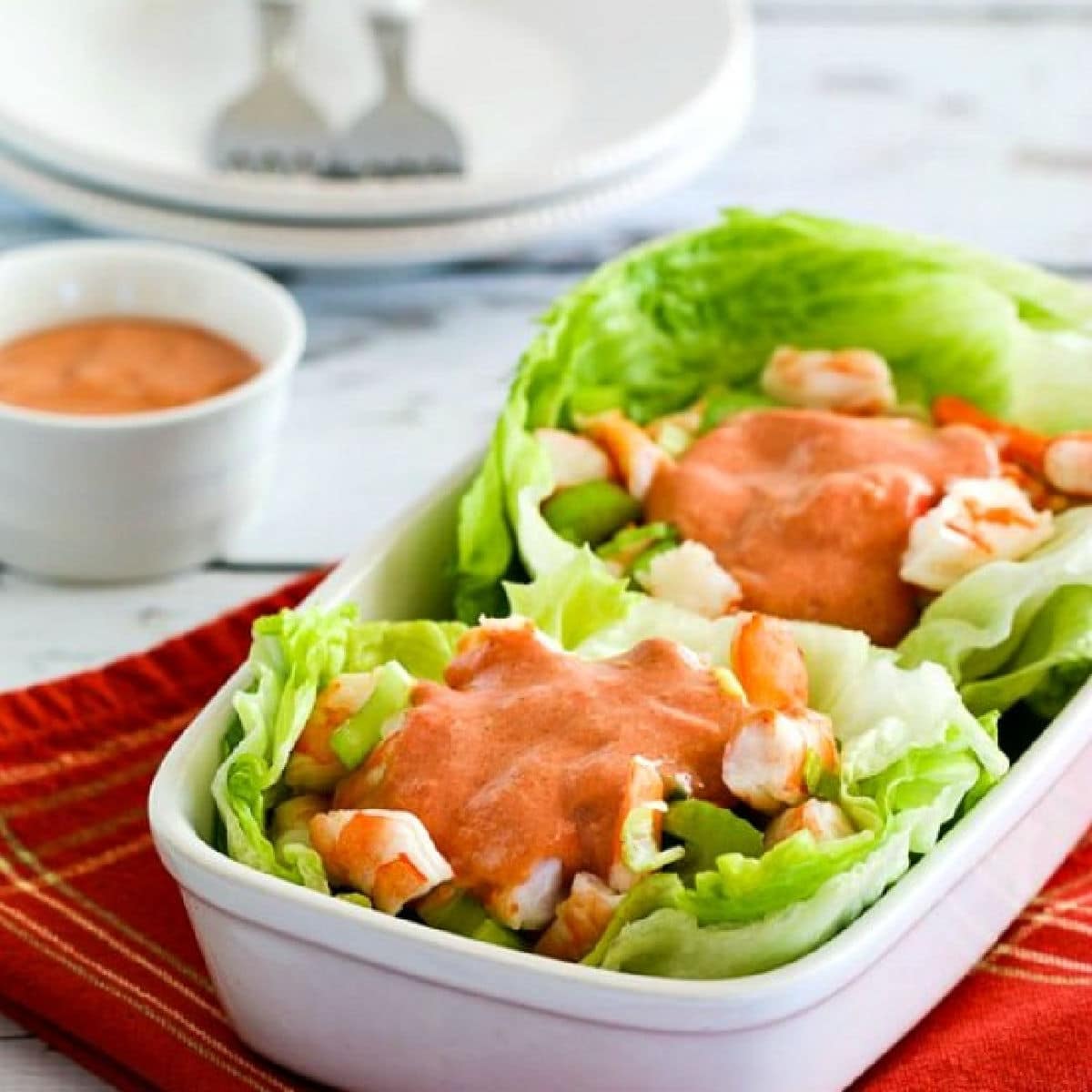 Square image for Shrimp lettuce wraps shown with two lettuce wraps in dish with cocktail sauce on the shrimp and on the side.