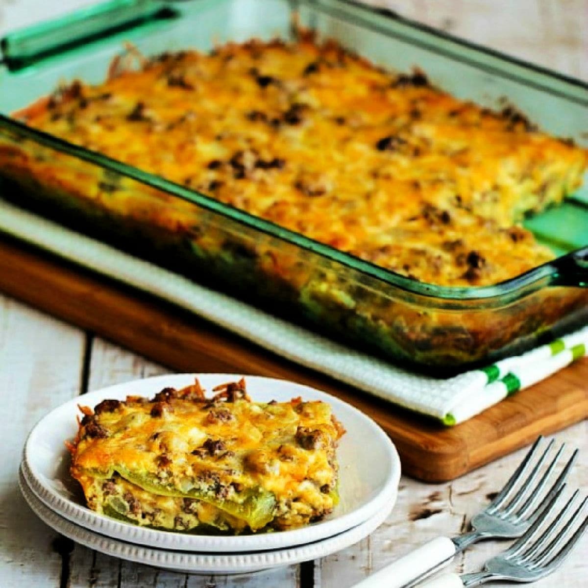 Beefy Cheesy Green Chile Bake shown in casserole dish with one piece on plate in front.