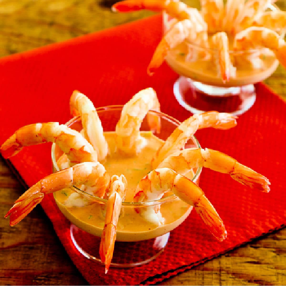 Shrimp Cocktail with Sriracha Cocktail Sauce shown in two cocktail glasses on red napkin.
