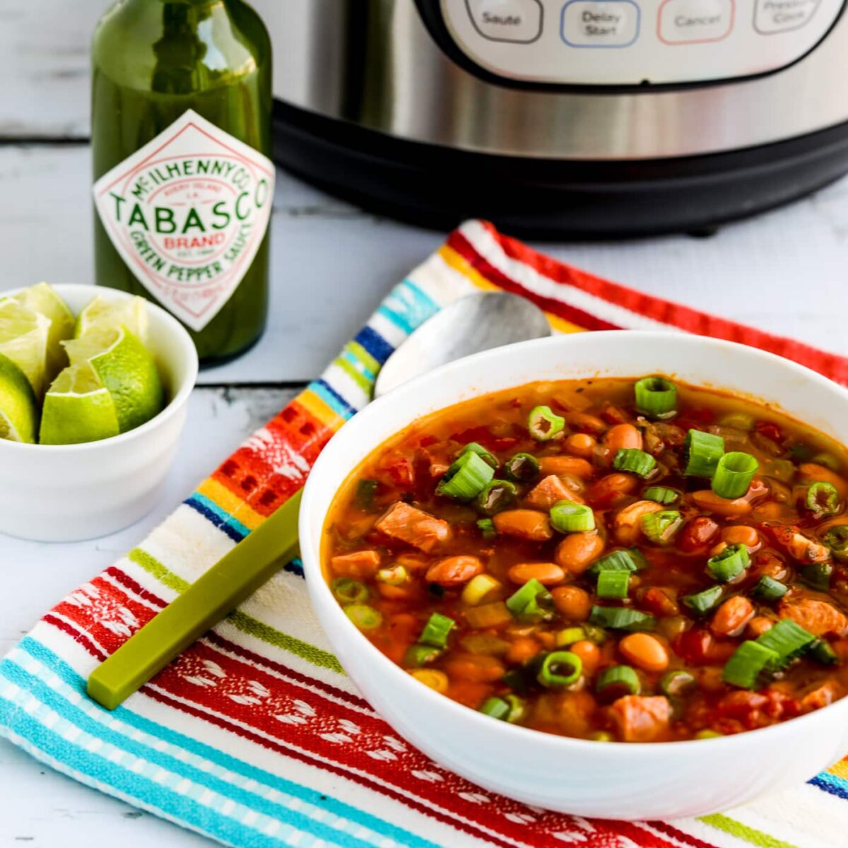 Square image for Instant Pot Ham and Bean Soup showing soup in serving bowl with limes on the side and Instant Pot in back.