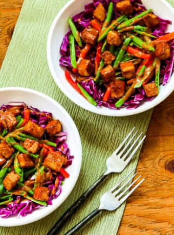 Square image of Cabbage Bowl with Tofu and Peanut Sauce shown with two bowls, forks, and green napkin.