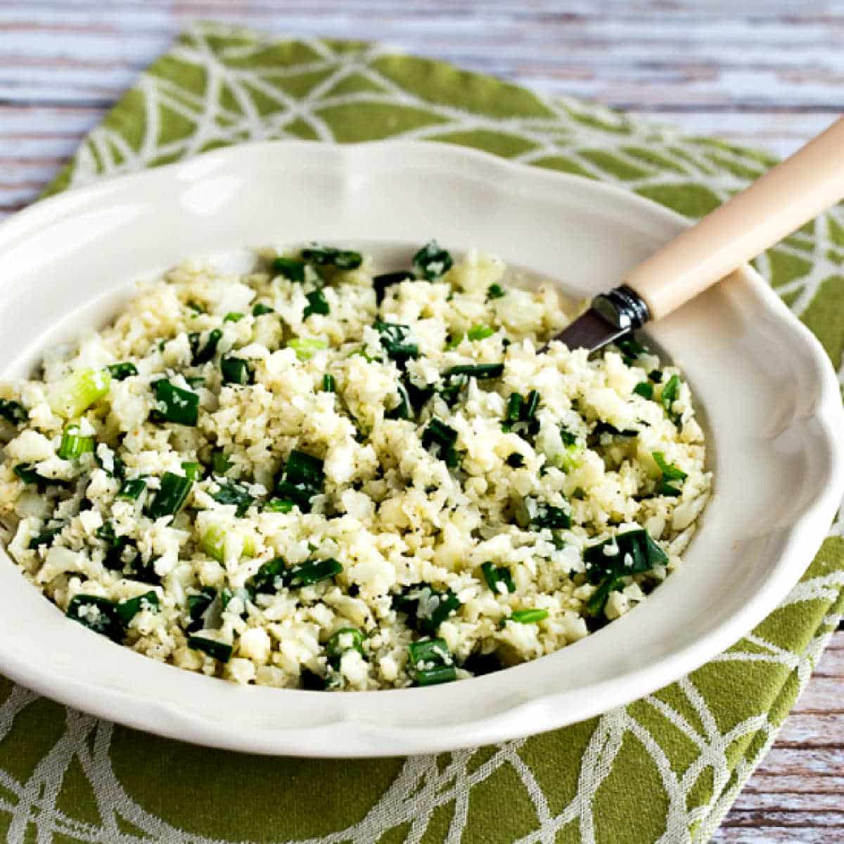 Square image for Easy Cauliflower Rice Recipe shown in serving bowl with spoon, or green-white napkin.