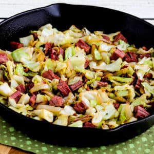Square image for Fried Cabbage with Corned Beef shown in cast-iron skillet on green napkin.