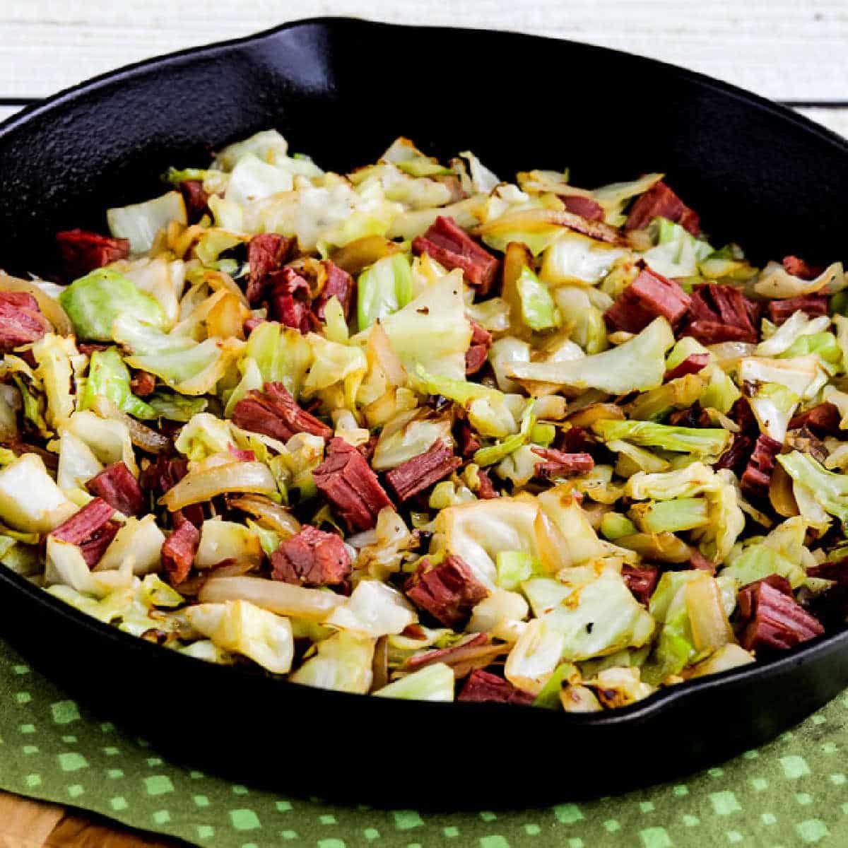 Square image for Fried Cabbage with Corned Beef shown in cast-iron skillet on green napkin.