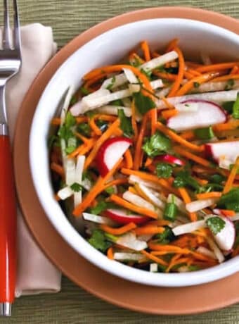 Square image of Jicama Carrot Radish Slaw shown in serving bowl on plate with orange fork.