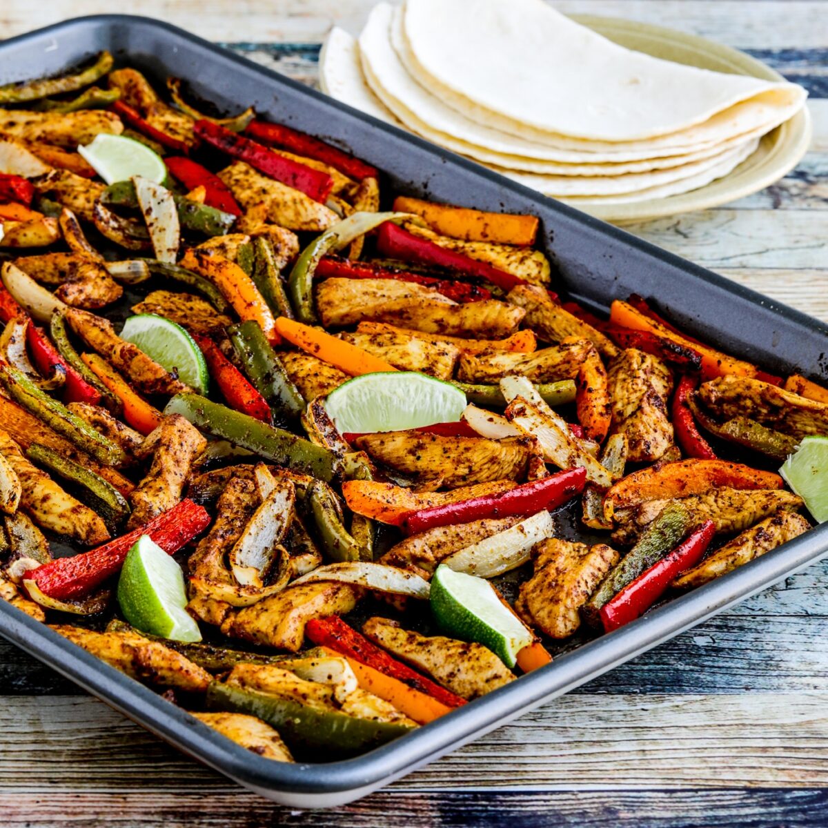 Square image of sheet bread chicken fajitas on a frying pan with tortillas on a plate