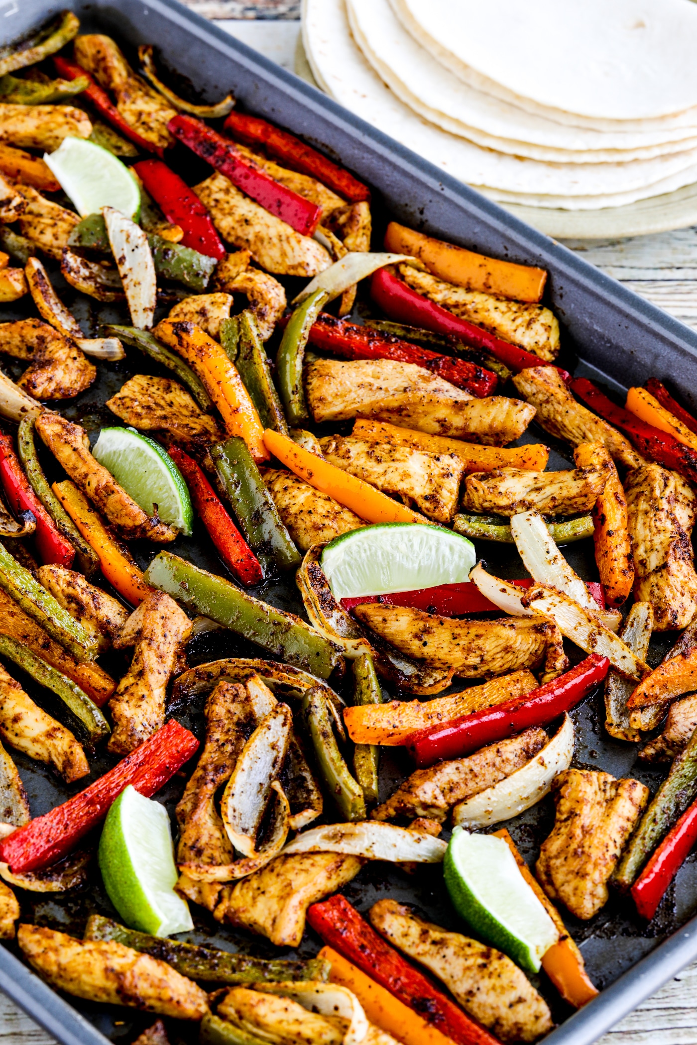 close-up photo of Sheet Pan Chicken Fajitas on pan with tortillas on plate