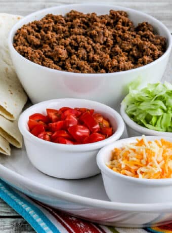 Square image of Instant Pot Taco Meat shown on serving platter with tortillas, taco meat, tomatoes, lettuce, and cheese.