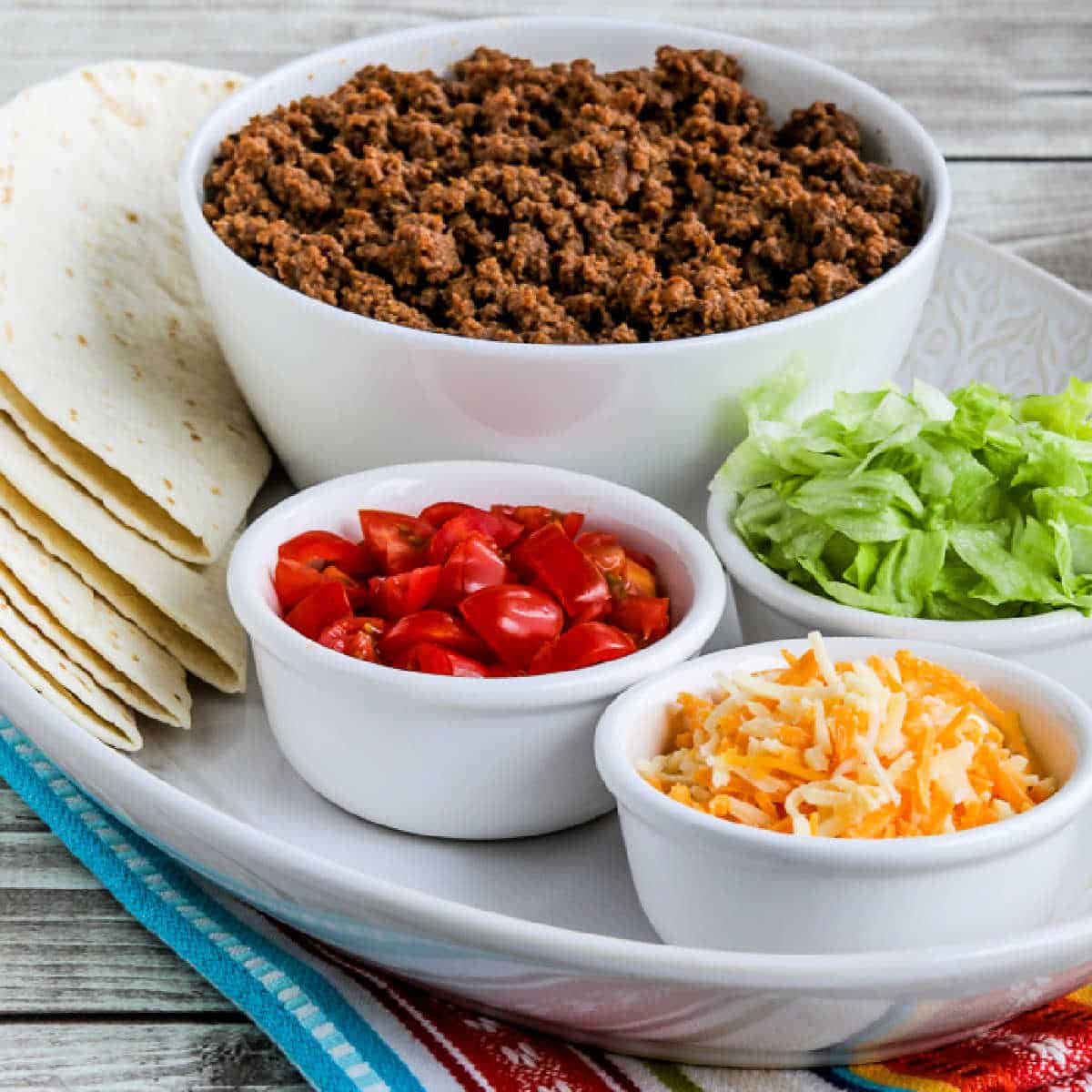 Square image of Instant Pot Taco Meat shown on serving platter with tortillas, taco meat, tomatoes, lettuce, and cheese.